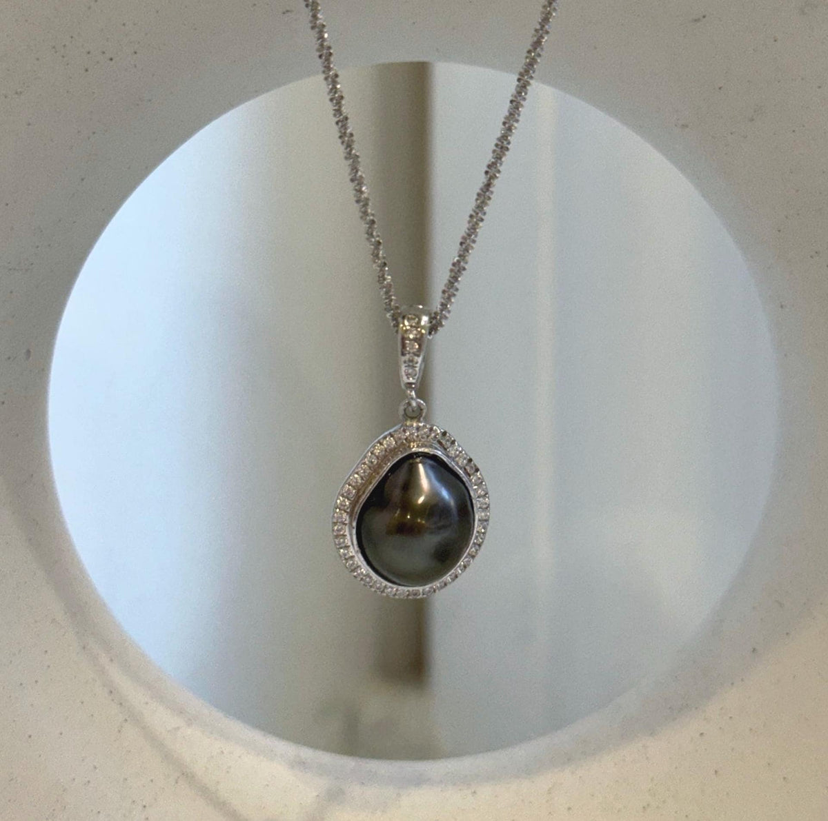 Dark Tahitian keshi pearl set within a curved sterling silver halo with clear stone accents.