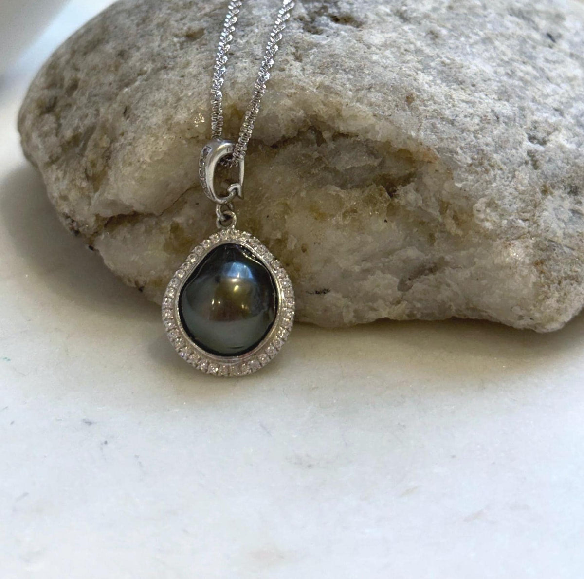 Dark Tahitian keshi pearl set within a curved sterling silver halo with clear stone accents.
