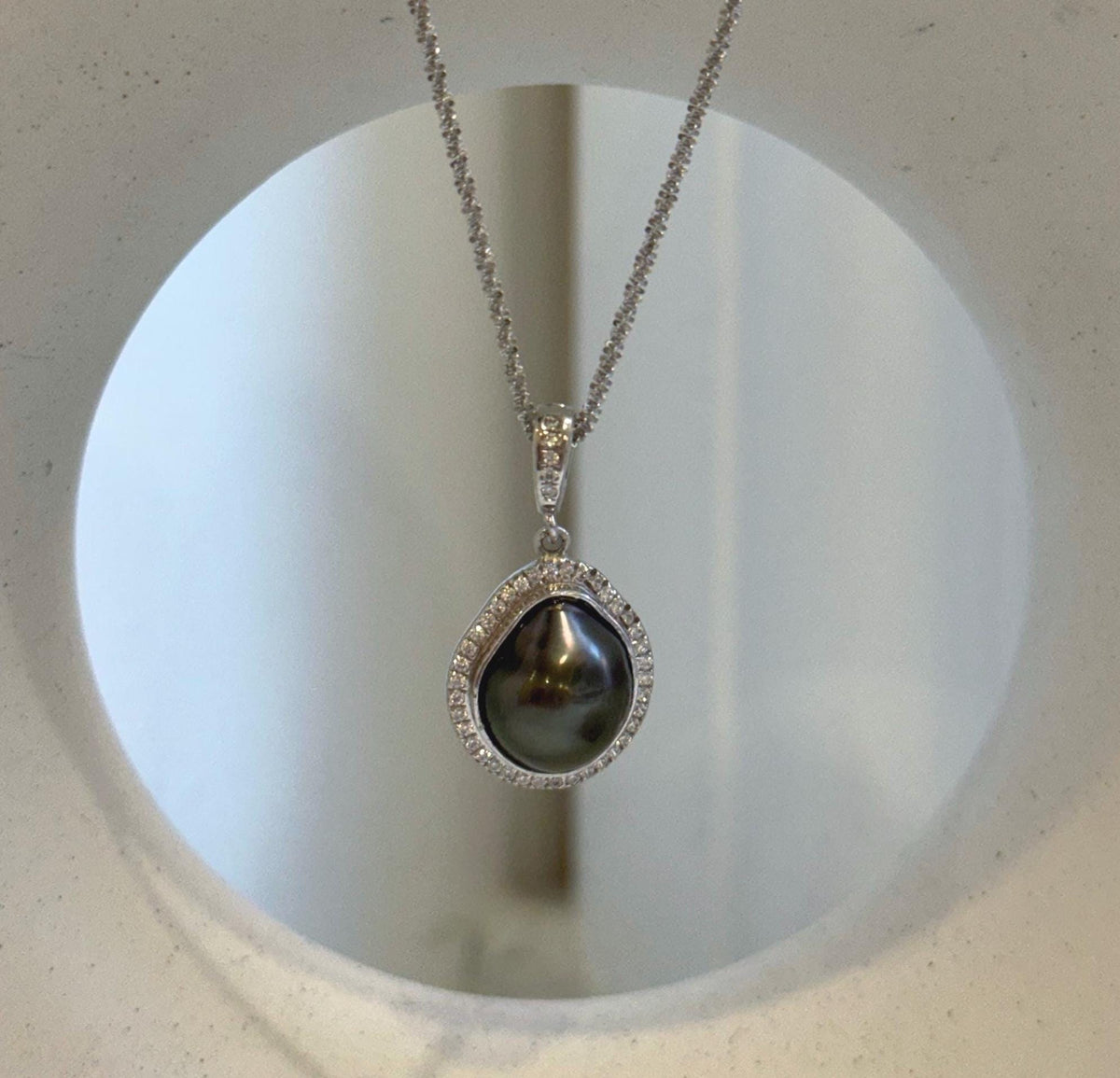 Irregular teardrop pearl pendant with a sparkling border and a silver chain.