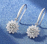 Round moissanite center stones framed by sparkling petal-like accents on silver drop earrings.