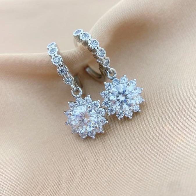 Round brilliant-cut moissanite centers surrounded by petal-like stones beneath silver hoops.