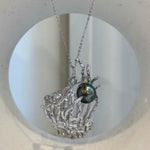 Sculptural coral branches surrounding a peacock green saltwater pearl.