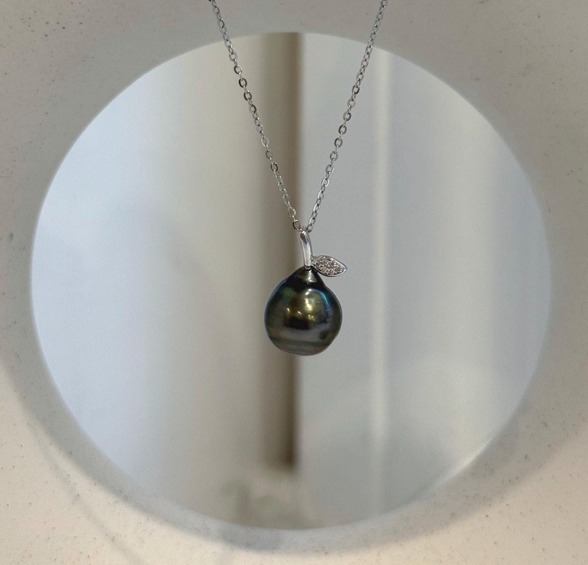 Hunter green Tahitian pearl pendant with a silver leaf detail, displayed on a cream necklace stand.