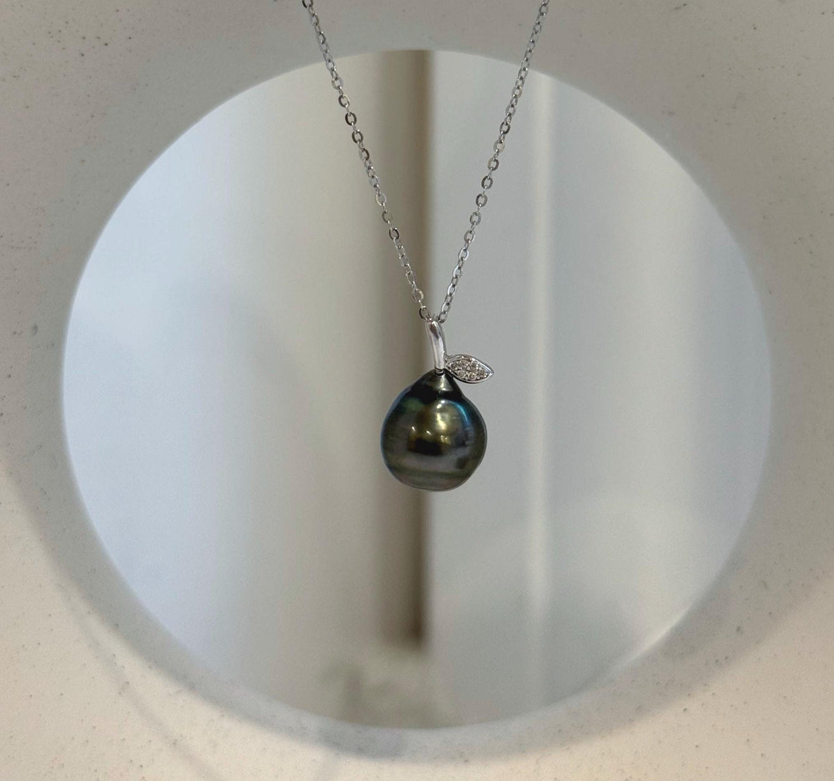 Tahitian pearl pendant suspended from a delicate silver chain with a sparkling leaf accent.