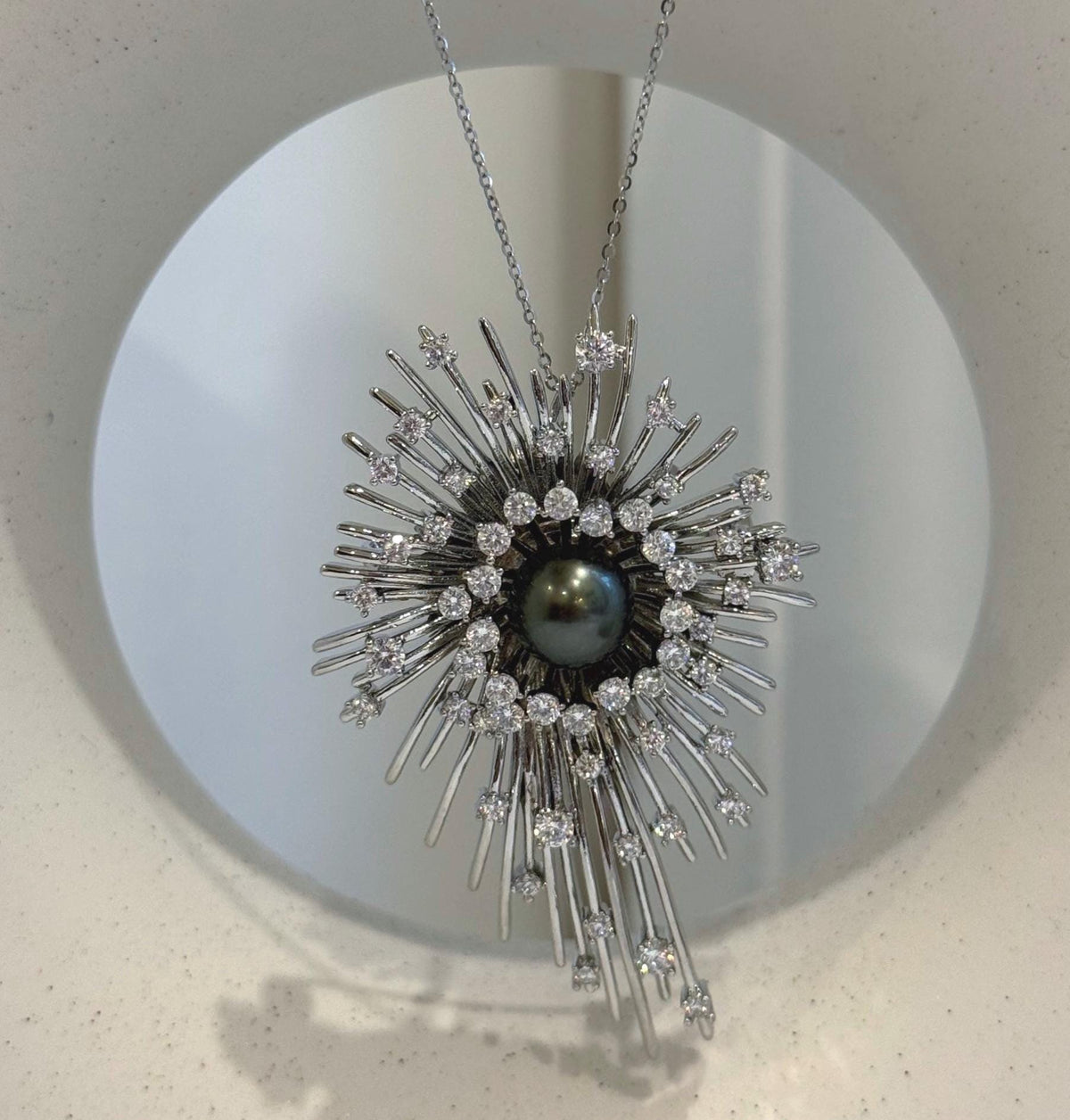 Black saltwater pearl set within a statement starburst brooch pendant