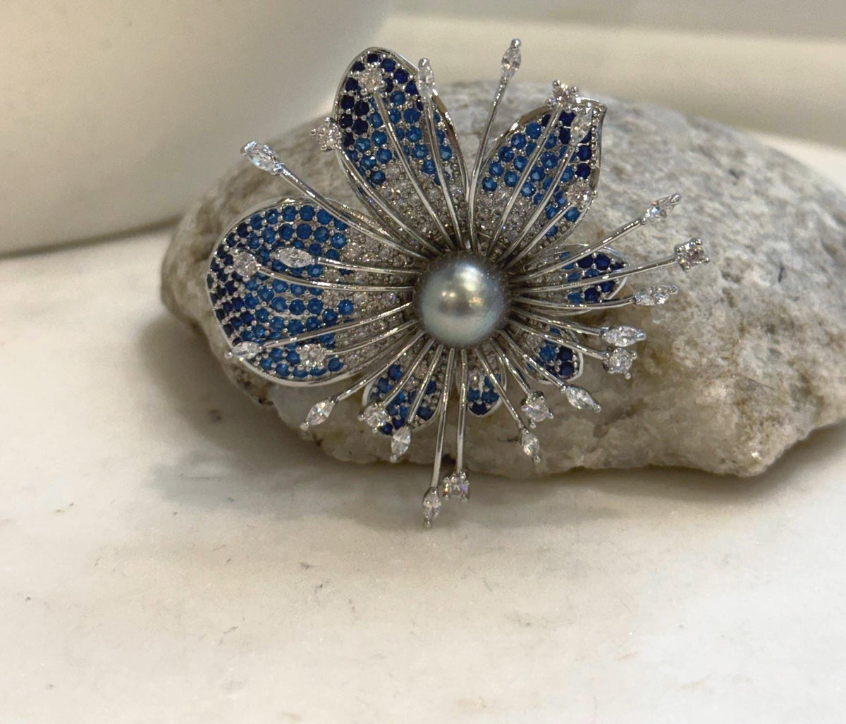 Gray pearl centerpiece surrounded by blue pavé-style petals and clear accents.