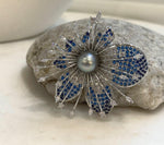 Statement pearl brooch displayed on a textured stone beside a white vase.