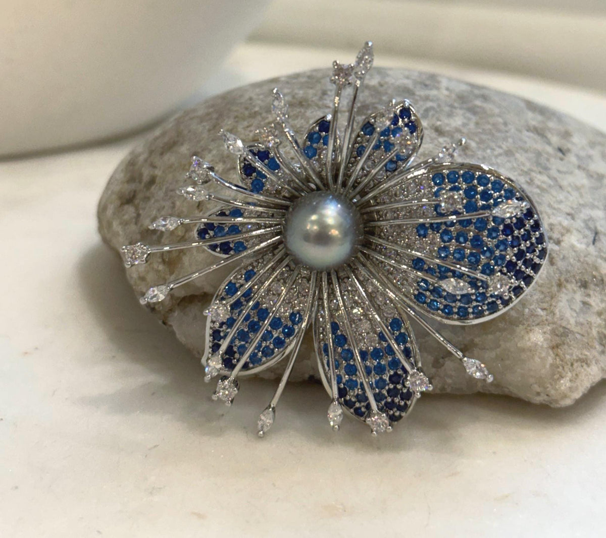 Statement pearl brooch displayed on a textured stone beside a white vase.