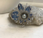 Silver-tone floral brooch with open petals and sparkling elongated details.