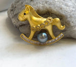 Gold-tone rocking horse brooch pendant with a lustrous dark gray Tahitian pearl beneath the horse.
