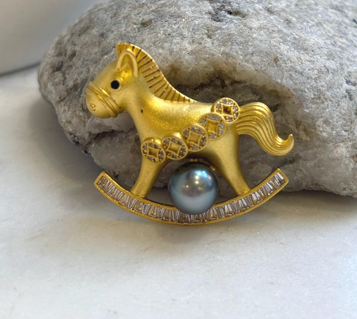 Rocking horse brooch with a textured gold-tone body, sculpted mane, and flowing curved tail.