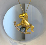 Dark Tahitian pearl nestled between the legs of a gold-tone rocking horse.