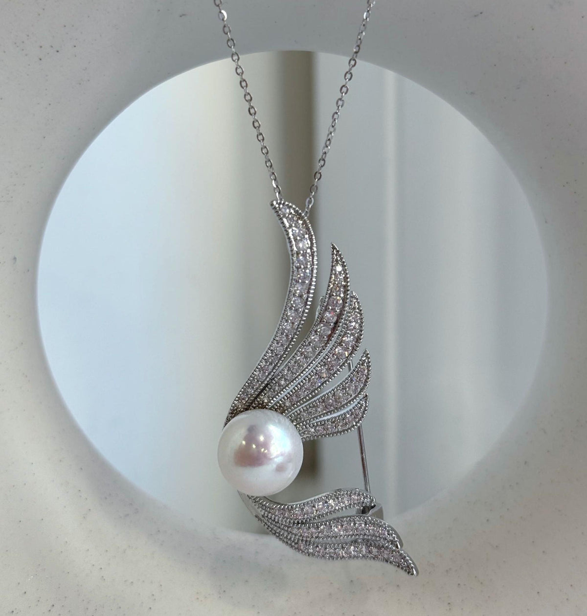 White pearl brooch displayed on a textured stone in natural window light.