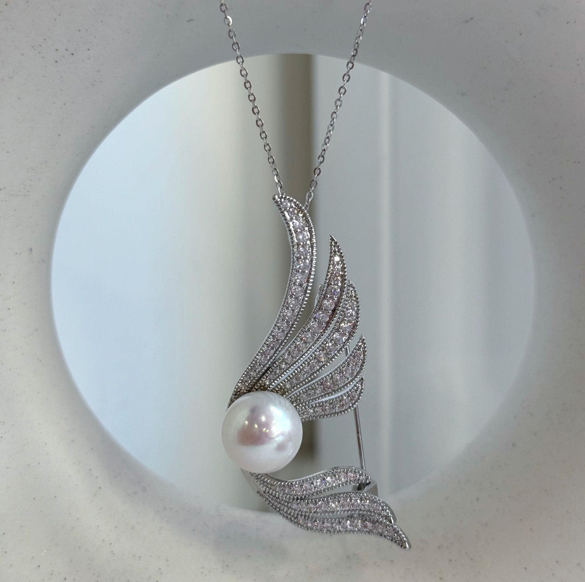 Silver-tone pearl brooch with rows of clear stones along flowing wings.