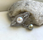 White and dark pearl brooch pendant displayed against a natural stone