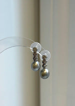 Elly’s 9mm gray pearl drop earrings with S925 sterling silver crisscross links, displayed on a clear stand.