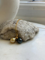 Gold-tone chain draped over a cream display bust, showcasing a twin-pearl pendant with golden South Sea and dark Tahitian pearls.