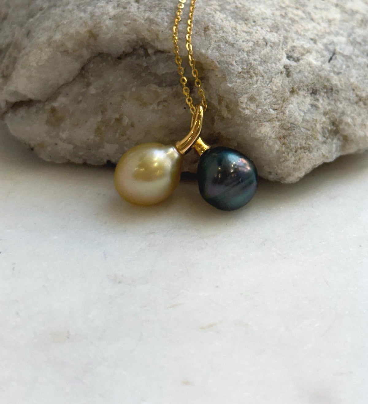 Twin-pearl pendant featuring a golden South Sea pearl on the left and a dark Tahitian pearl on the right, suspended from a delicate gold-tone chain.