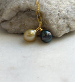 Twin-pearl pendant featuring a golden South Sea pearl on the left and a dark Tahitian pearl on the right, suspended from a delicate gold-tone chain.