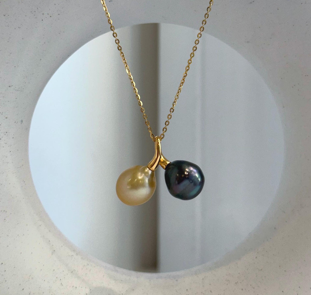Two-pearl necklace with contrasting golden and dark green tones, displayed against a cream jewelry bust with an oval opening.