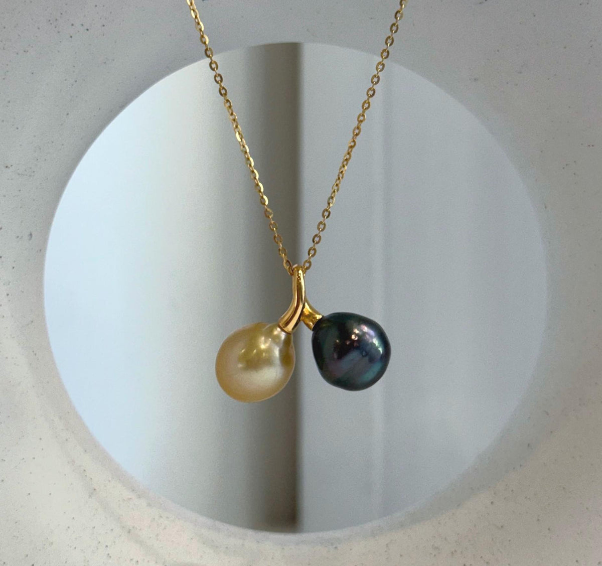 Pearl necklace featuring a softly rounded golden pearl beside a dark Tahitian pearl with visible green and purple reflections.